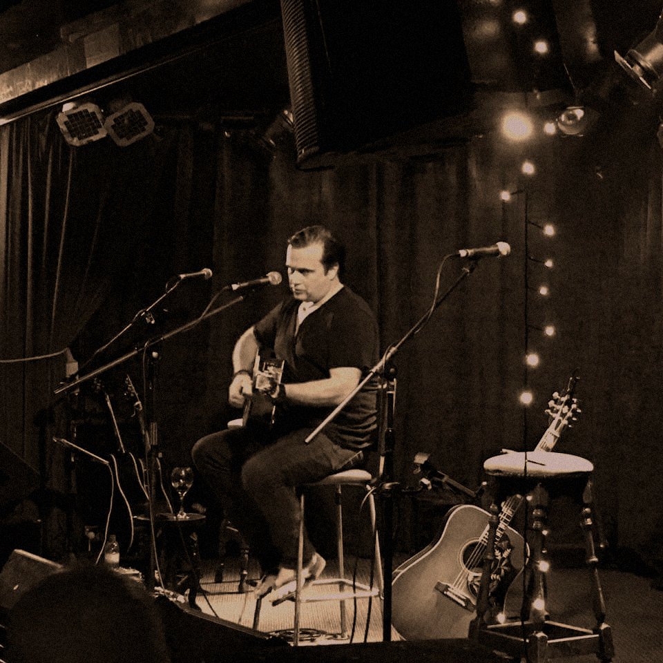 Jason Kearney Jason Kearney with a guitar in a small, dimly lit room